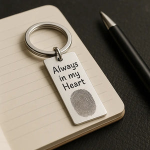 Personalized fingerprint keychain with engraved text placed on a notebook beside a pen