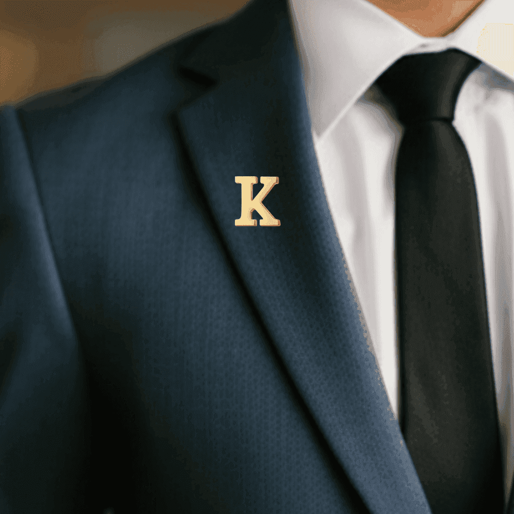 Elegant gold initial letter brooch pin worn on a suit jacket lapel for a stylish look