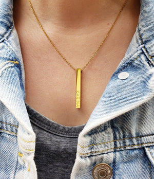 Gold Bar Name Necklace with engraved letters worn with denim jacket and gray shirt