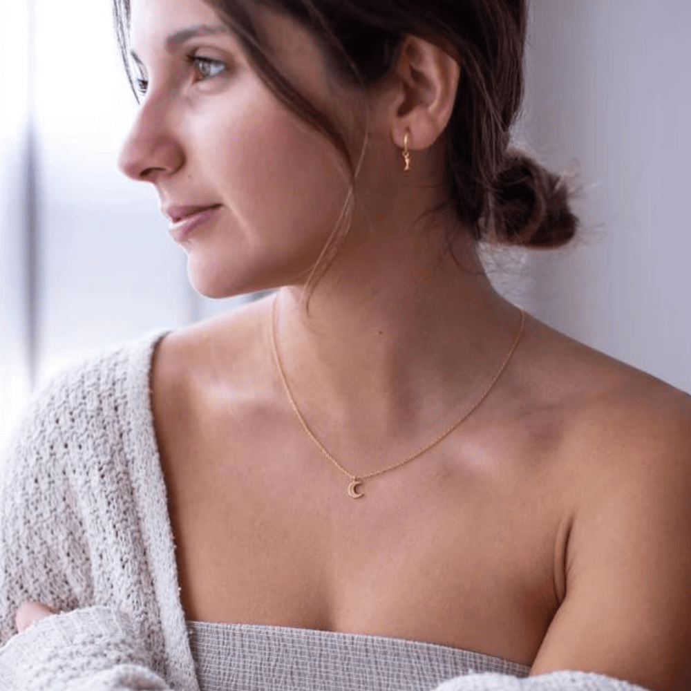 Woman wearing a delicate half moon necklace silver or gold plated with matching small hoop earrings