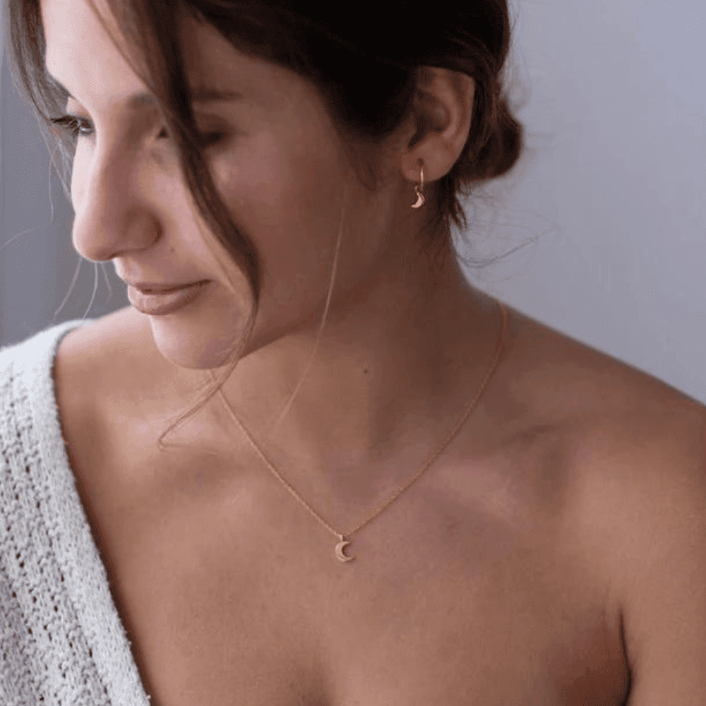 Woman wearing a delicate half moon necklace silver or gold plated with matching crescent earrings