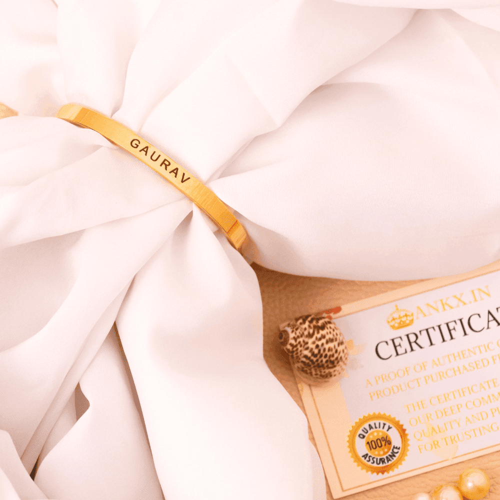 Gold Ankx.in name bracelet with personalized engravings on a soft white fabric backdrop