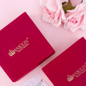 Ankx.in red jewelry boxes with gold logo branding placed near pink roses and a Name Necklace Crown And Heart card