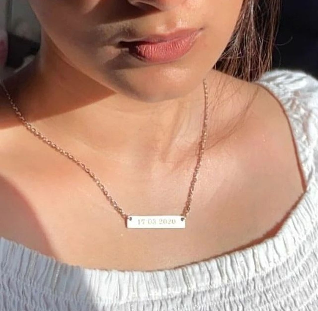 Ankx.in name necklace plate with engraved date worn by woman in white top