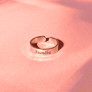 Silver adjustable name ring engraved with Anandhu on a pink background from Ankx.in