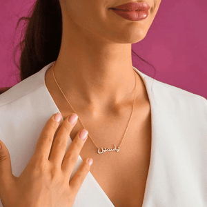 Elegant gold Urdu Name Necklace worn by woman with white top and pink background