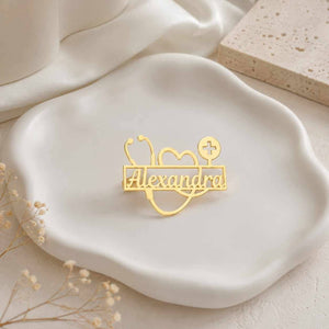 Gold doctor brooch with name Alexandra on ceramic plate flatlay