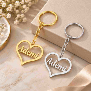 Gold and silver personalized heart keychains with the name Ademi displayed on a light beige gift box setting.
