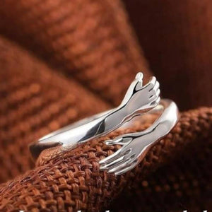 Silver hug ring with intertwined hands design, symbolizing love and connection