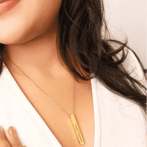Woman wearing a gold personalized bar necklace engraved with "Love Forever" close to her neckline
