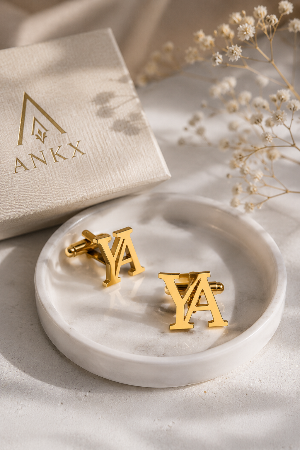 Personalized gold letter cufflinks in marble dish beside ANKX gift box and dried flowers