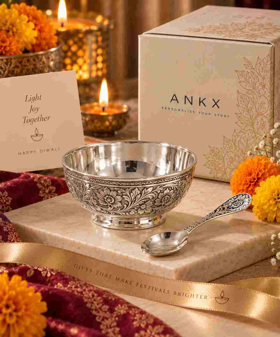 Premium silver bowl and spoon Diwali gift set displayed on a marble pedestal with marigold flowers, glowing diyas, festive décor, and elegant ANKX gift packaging