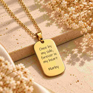 Gold personalized dog tag necklace with custom “Once by my side, forever in my heart” and “Marley” engraving on a luxury beige stone surface.