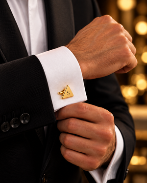 Personalized gold triangular cufflink with black engraved S initial on a white French cuff and black suit