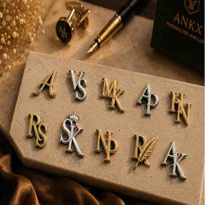 Gold and silver monogram initial pins displayed with cufflinks and a fountain pen.