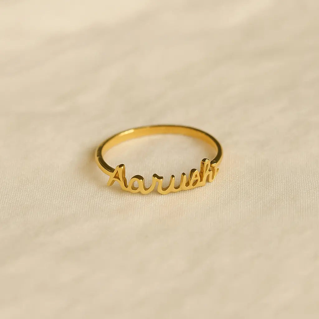 Gold custom name ring with “Aarushi” text placed on a soft beige fabric background