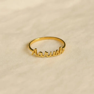 Gold custom name ring with “Aarushi” text placed on a soft beige fabric background