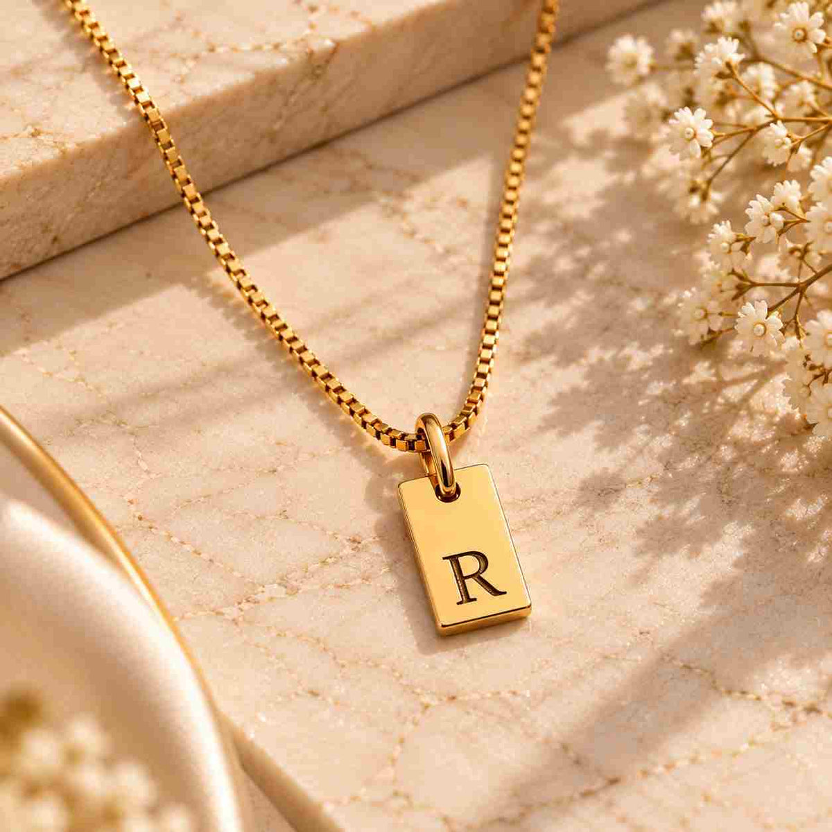Gold personalized initial R necklace with black engraved letter R displayed on ivory marble