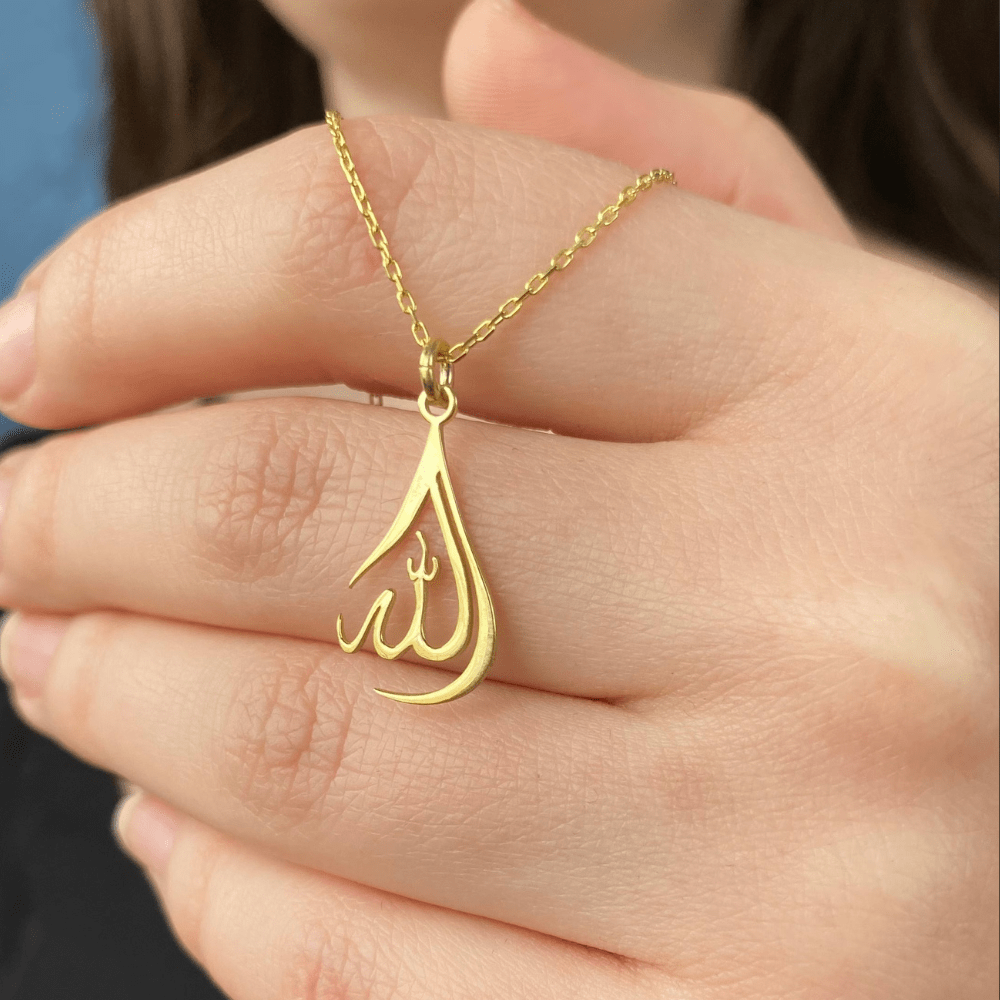 Delicate Allah Necklace Pendant Gold Plated hanging on a gold chain held by hand