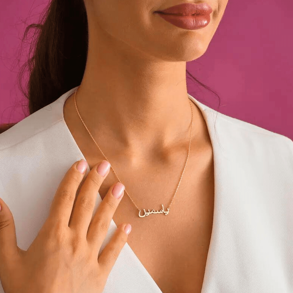 Elegant gold Urdu Name Necklace worn by woman with white top and pink background