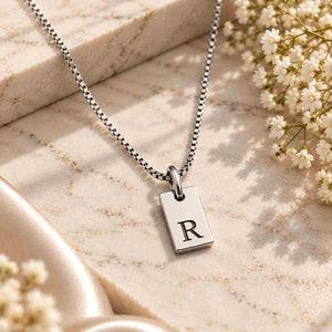 Silver personalized initial R necklace with black engraved letter R displayed on ivory marble