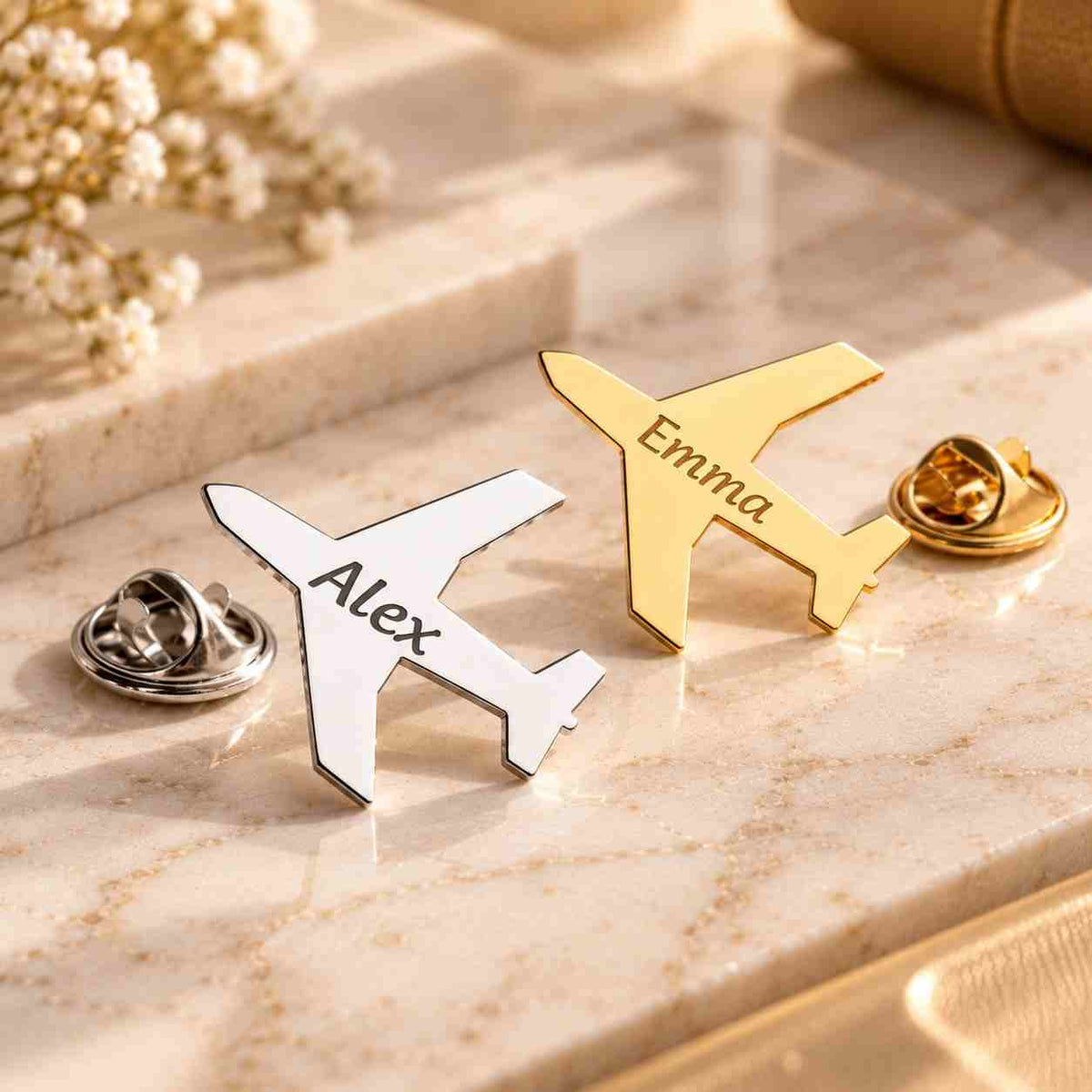 Personalized silver and gold airplane brooches engraved with Alex and Emma displayed together