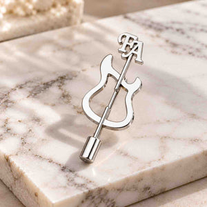 Silver personalized guitar brooch displayed on a light beige marble surface with FA initials