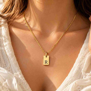 Woman wearing a gold personalized R initial necklace with black engraved pendant
