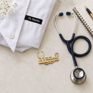 CUSTOM DOCTOR PIN in gold with engraved name Dr. A. Bhattacharya next to a white lab coat and stethoscope