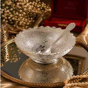 Ornate silver textured bowl and spoon set on a mirrored tray