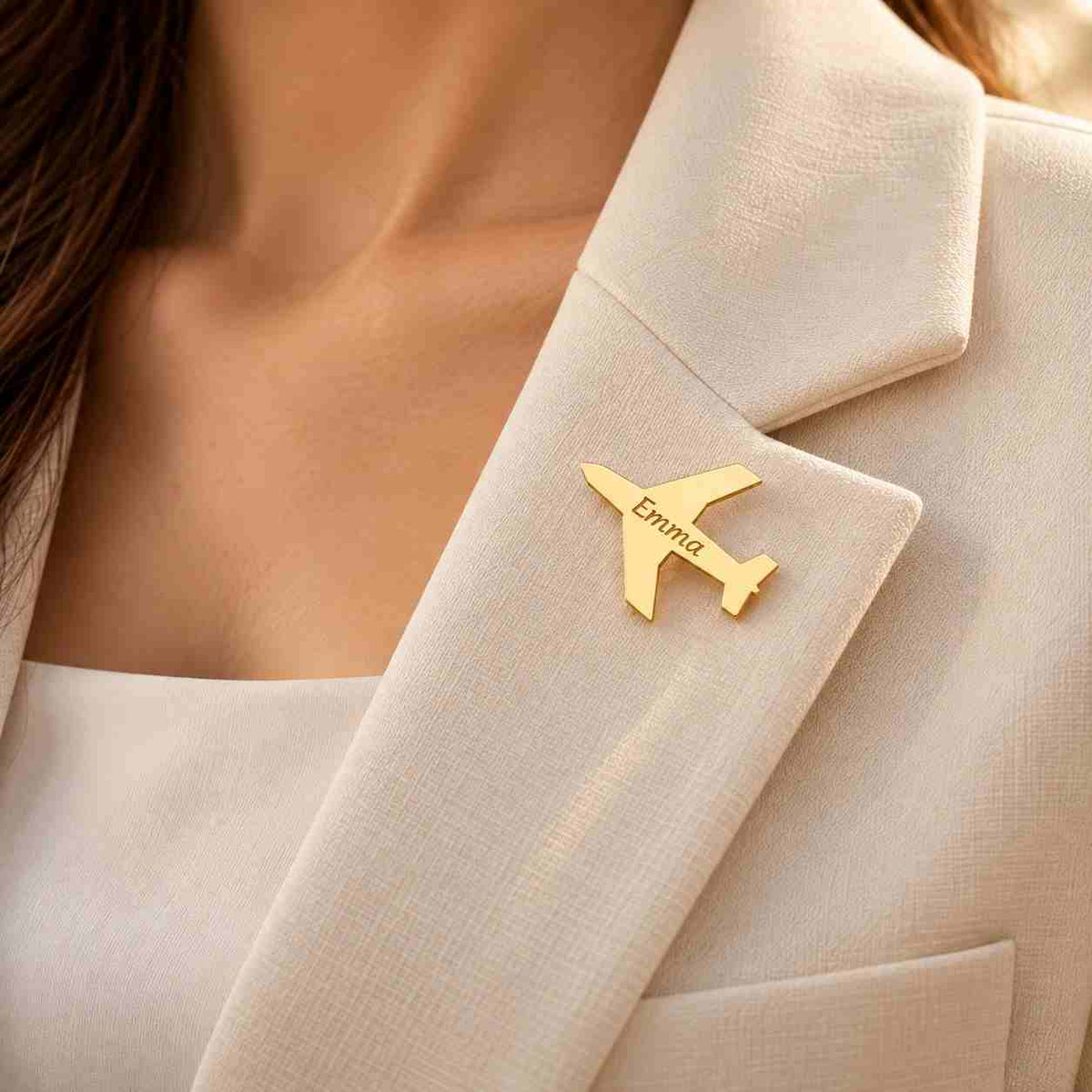 Personalized gold airplane brooch engraved with Emma worn on an elegant cream blazer