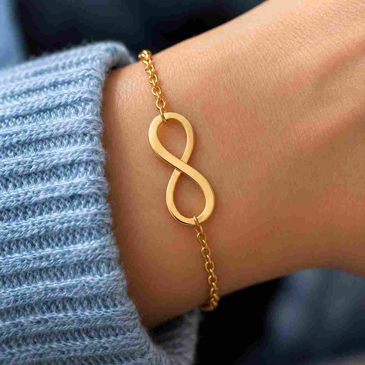Gold infinity bracelet worn on a wrist with a light blue knitted sleeve