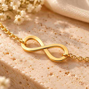Close-up of a plain gold infinity bracelet on a beige stone surface