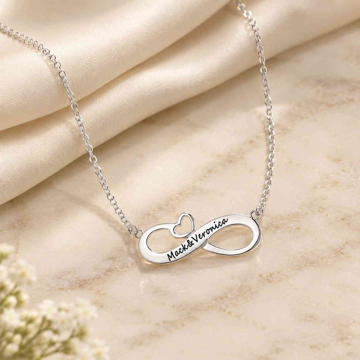 Personalized silver infinity couple name necklace engraved with Mack & Veronica on an ivory marble surface