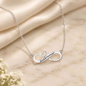 Personalized silver infinity couple name necklace engraved with Mack & Veronica on an ivory marble surface