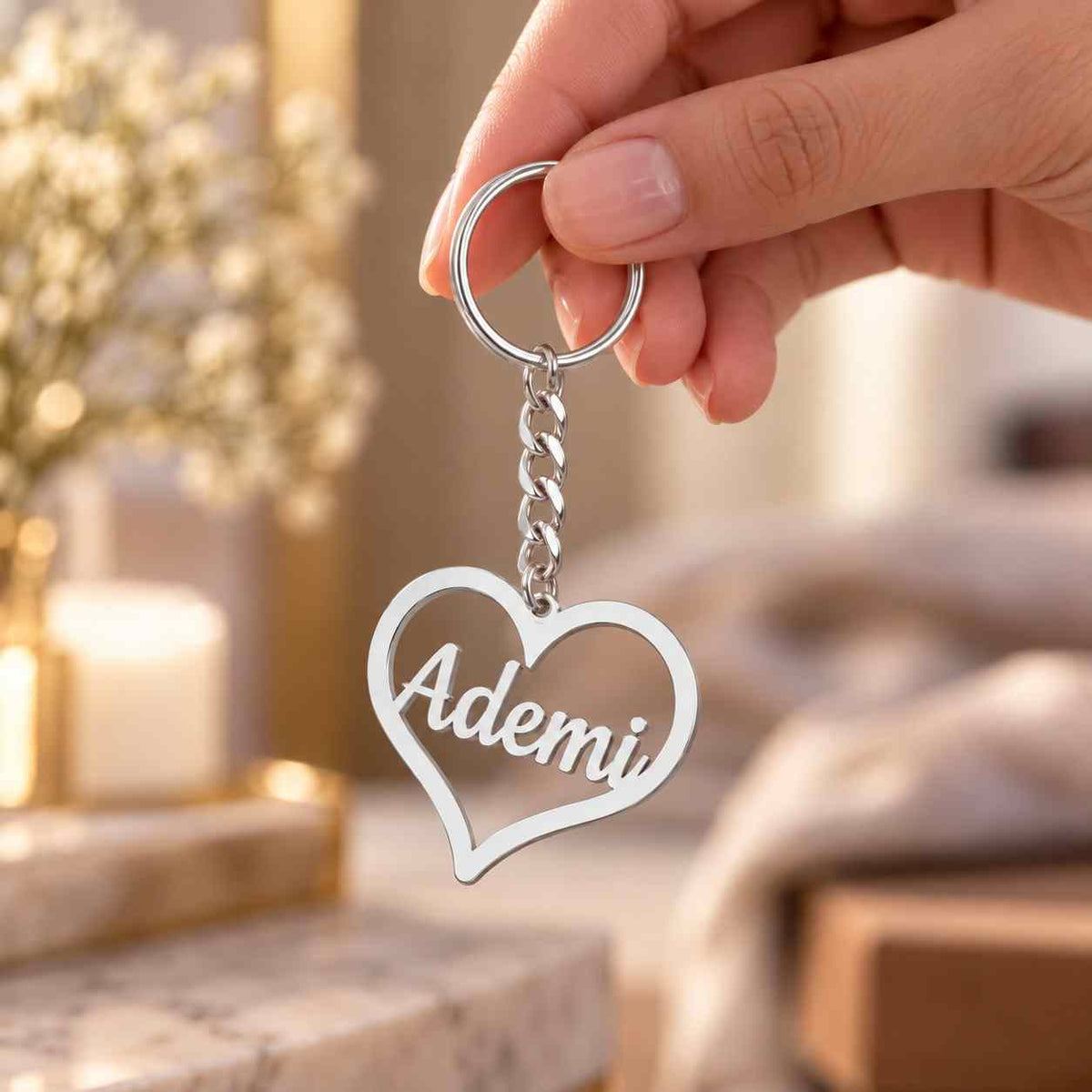 Silver personalized heart keychain with the name Ademi held by hand against a softly blurred light background.