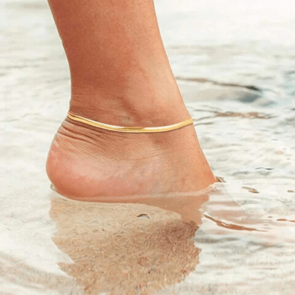 Minimal silver anklet for women worn in shallow water, showcasing elegant simplicity