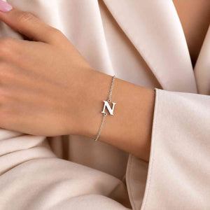 Silver N initial bracelet worn on wrist with delicate chain and serif N charm against a cream blazer