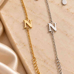 Gold and silver N initial bracelets displayed vertically side by side on cream marble
