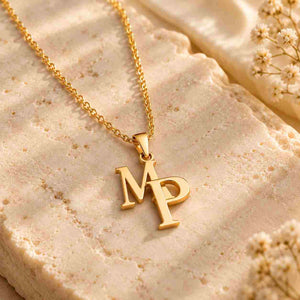Gold interlocking M P initial necklace on cream marble with white flowers