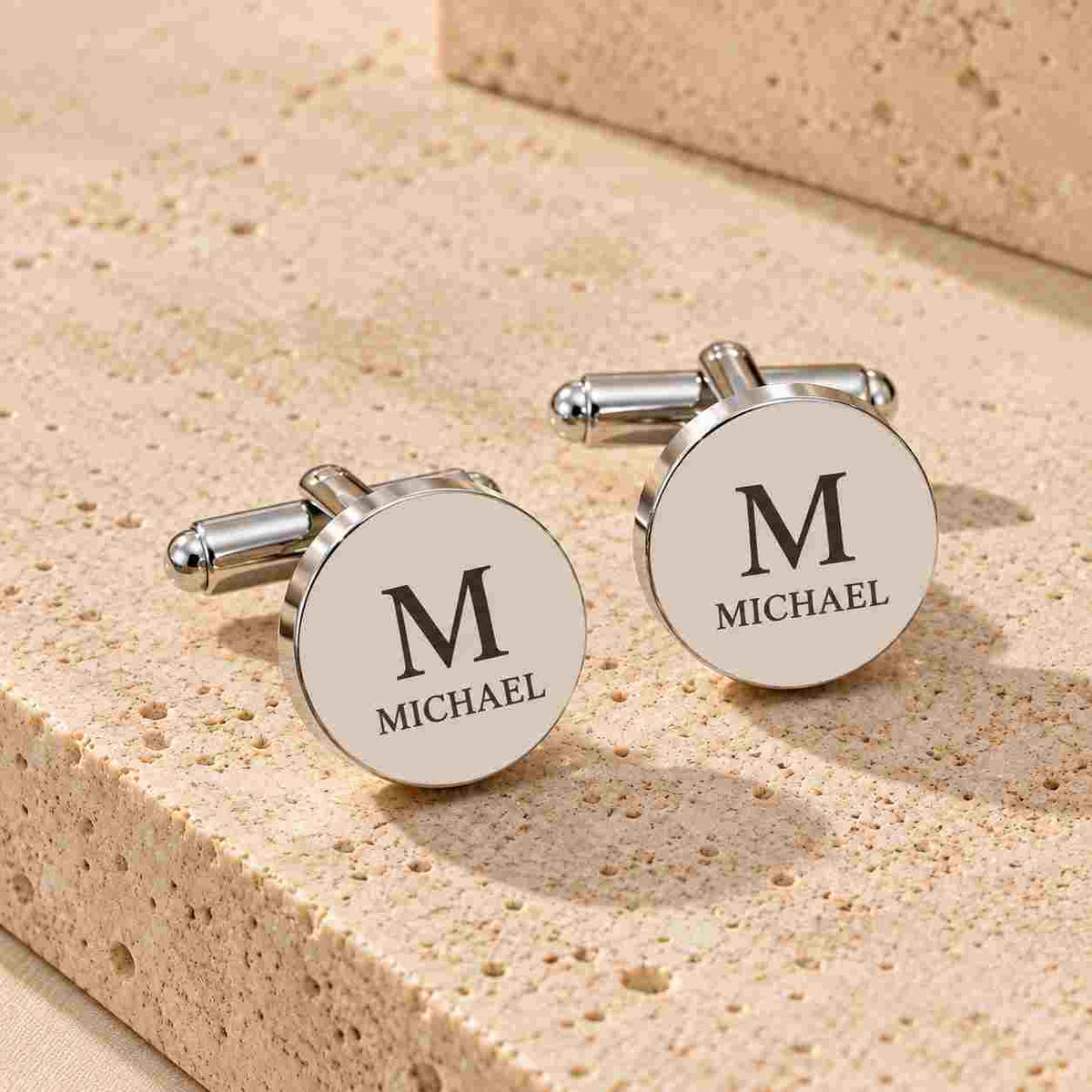 Personalized silver round cufflinks with engraved initial and name on a wedding surface