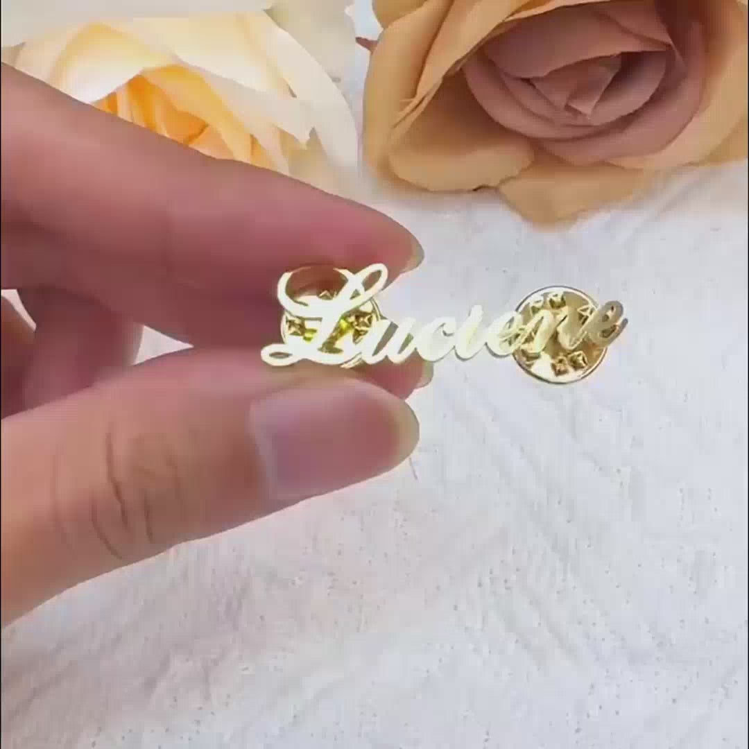 Person pinning a gold custom name brooch that reads Luciene onto a black denim jacket.