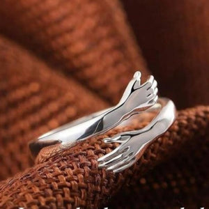 Silver hug ring with intertwined hands design, symbolizing love and connection