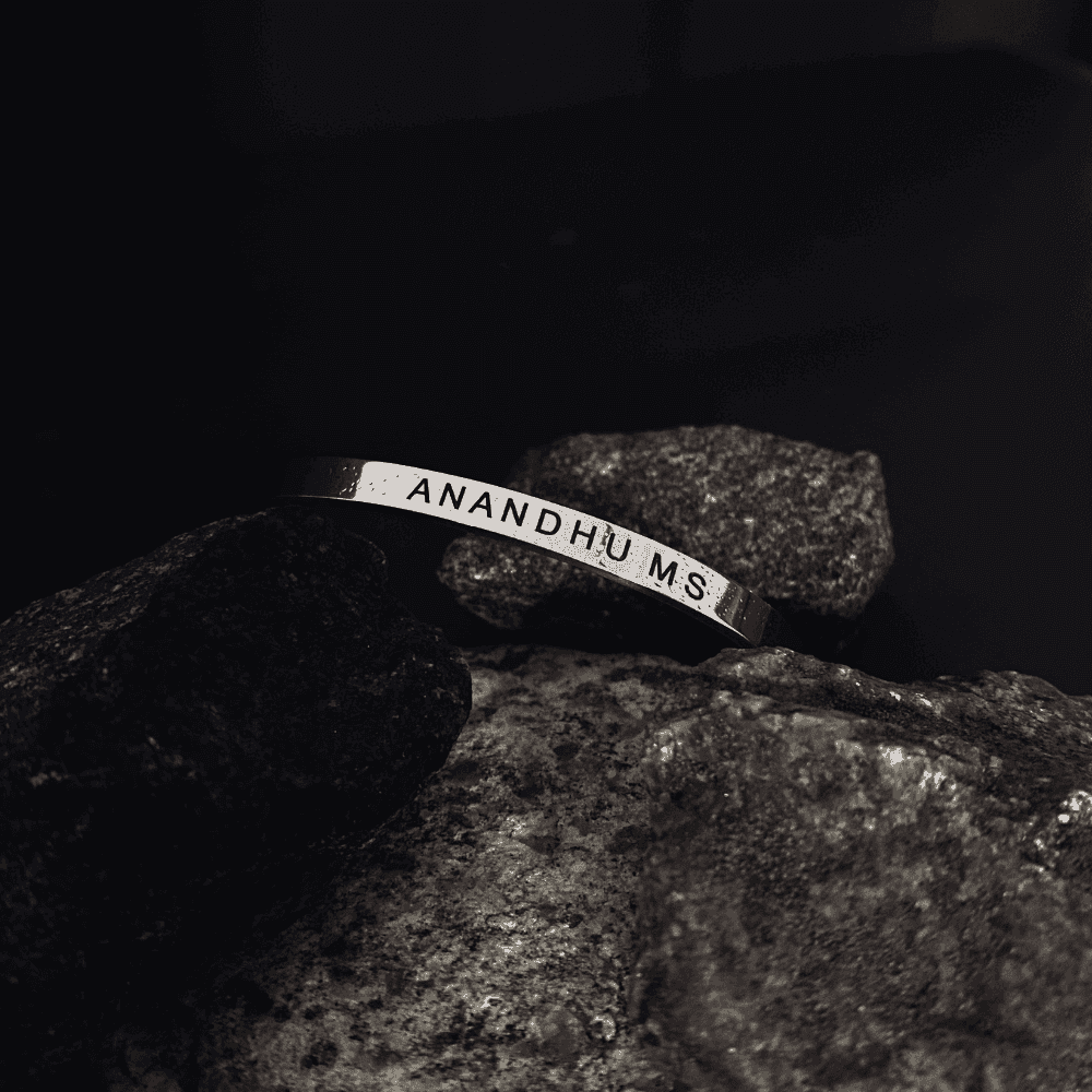 Personalized Silver Name Bracelet engraved with Anandhu MS placed on a dark aesthetic rock.